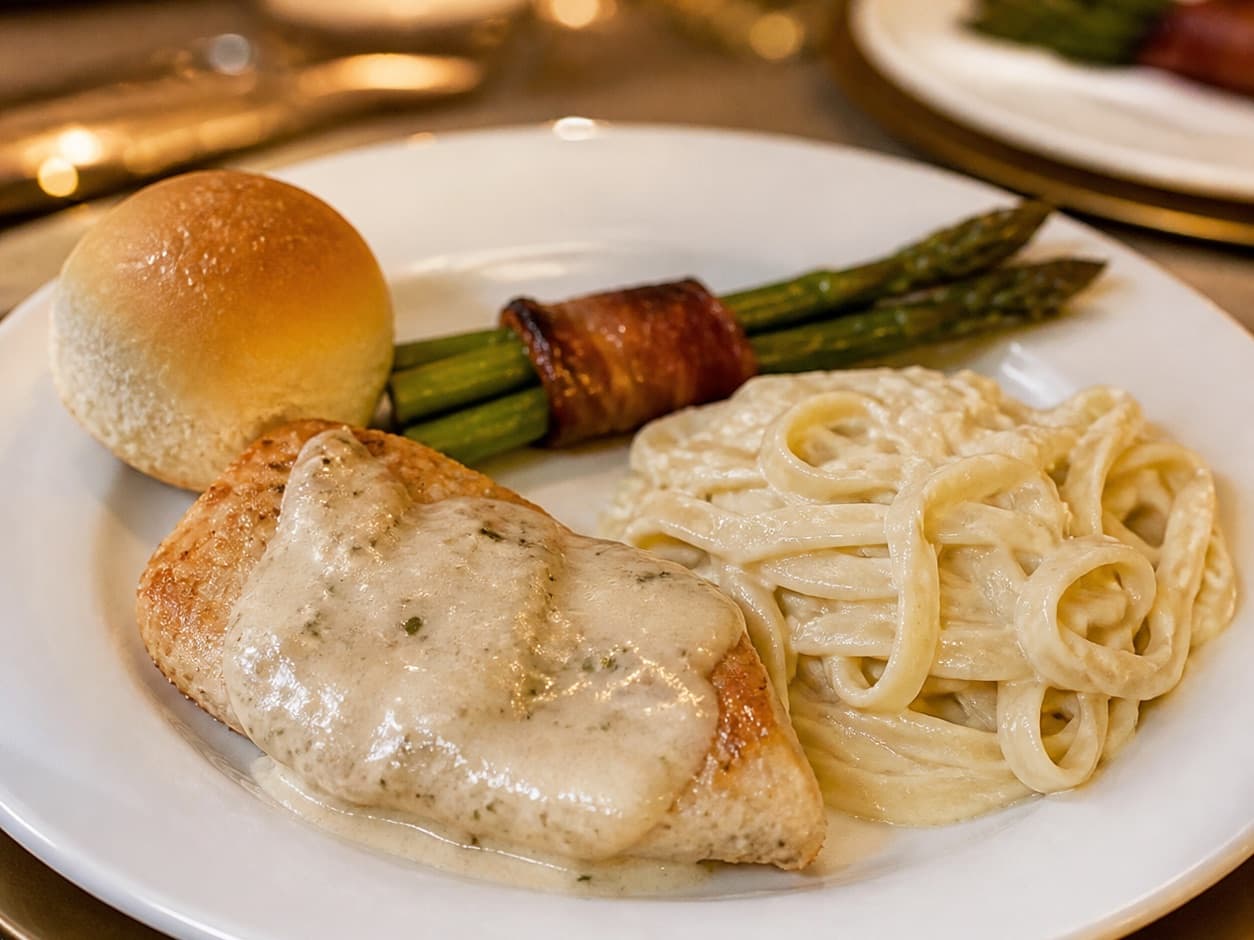 Elegant plated chicken dinner with bacon-wrapped asparagus on a candlelit celebration table